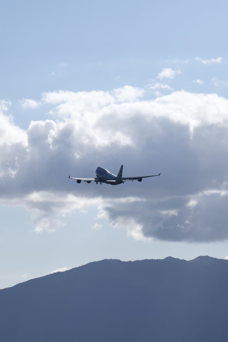 An airliner climbing away over clouds and mountains